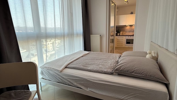 Een moderne slaapkamer met een bed, een stoel, een vloerkleed en een stadszicht door grote ramen.