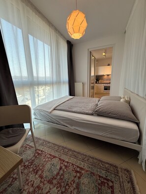 Un dormitorio moderno con cama, una silla, un tapete y vistas de la ciudad a través de amplias ventanas.