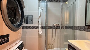 Een kleine hotelbadkamer met een wasmachine, een douche met glazen wanden en een toilet.