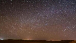 Een sterrenhemel boven een woestijnlandschap met verschillende verlichte tenten.