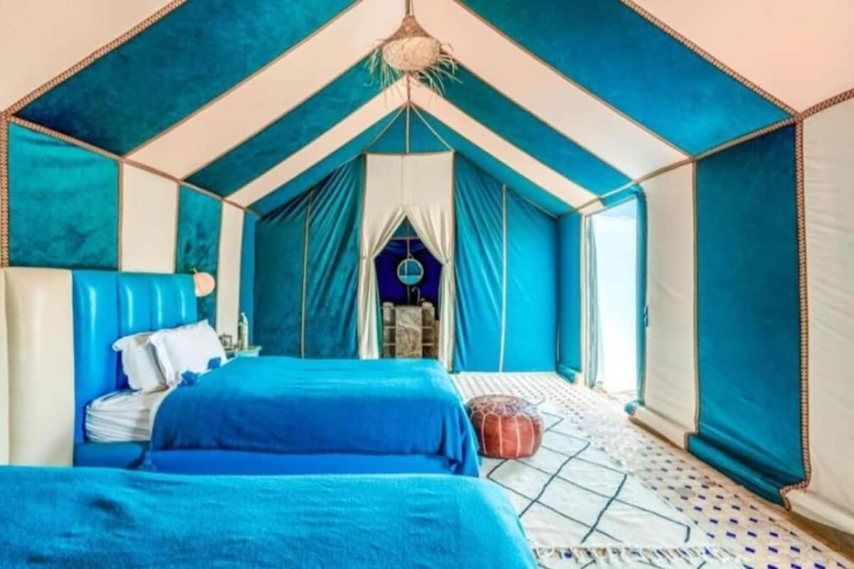 Um quarto tipo tenda com duas camas, um candeeiro pendente e um soalho estampado.