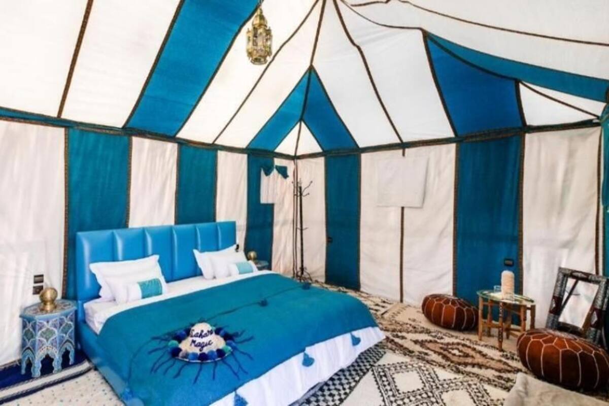 Um quarto com tenda, uma cama, almofadas, uma pequena mesa e um lustre.