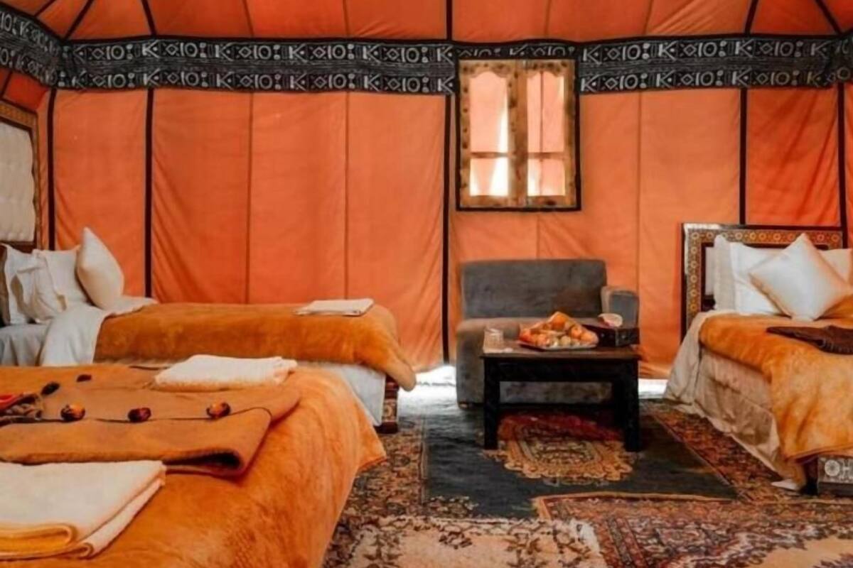 Uma tenda com duas camas, uma mesinha e uma janela.