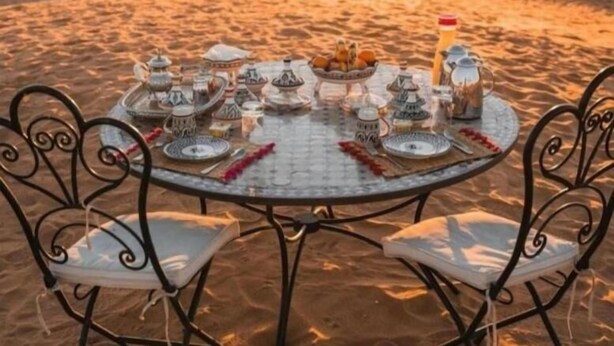 Een woestijnlandschap met een ronde tafel gedekt voor een maaltijd, omringd door woestijntenten.