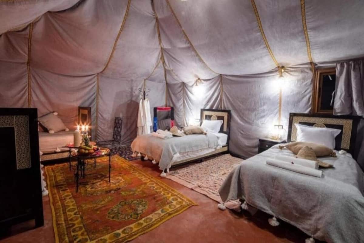 Um quarto tipo tenda com duas camas, uma mesinha com um abajur e um tapete decorativo.