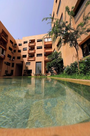 Ein Innenhof mit klarem Pool, ein mehrstöckiges Gebäude mit Balkonen und üppigem Grün.