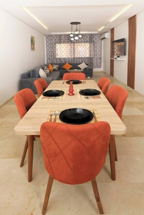 Ein Essbereich mit einem langen Holztisch, orange gepolsterten Stühlen und einem modernen Kronleuchter.