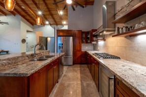 Une cuisine moderne dotée de plans de travail en granit, d’appareils électroménagers en acier inoxydable, d’armoires en bois et de luminaires suspendus.