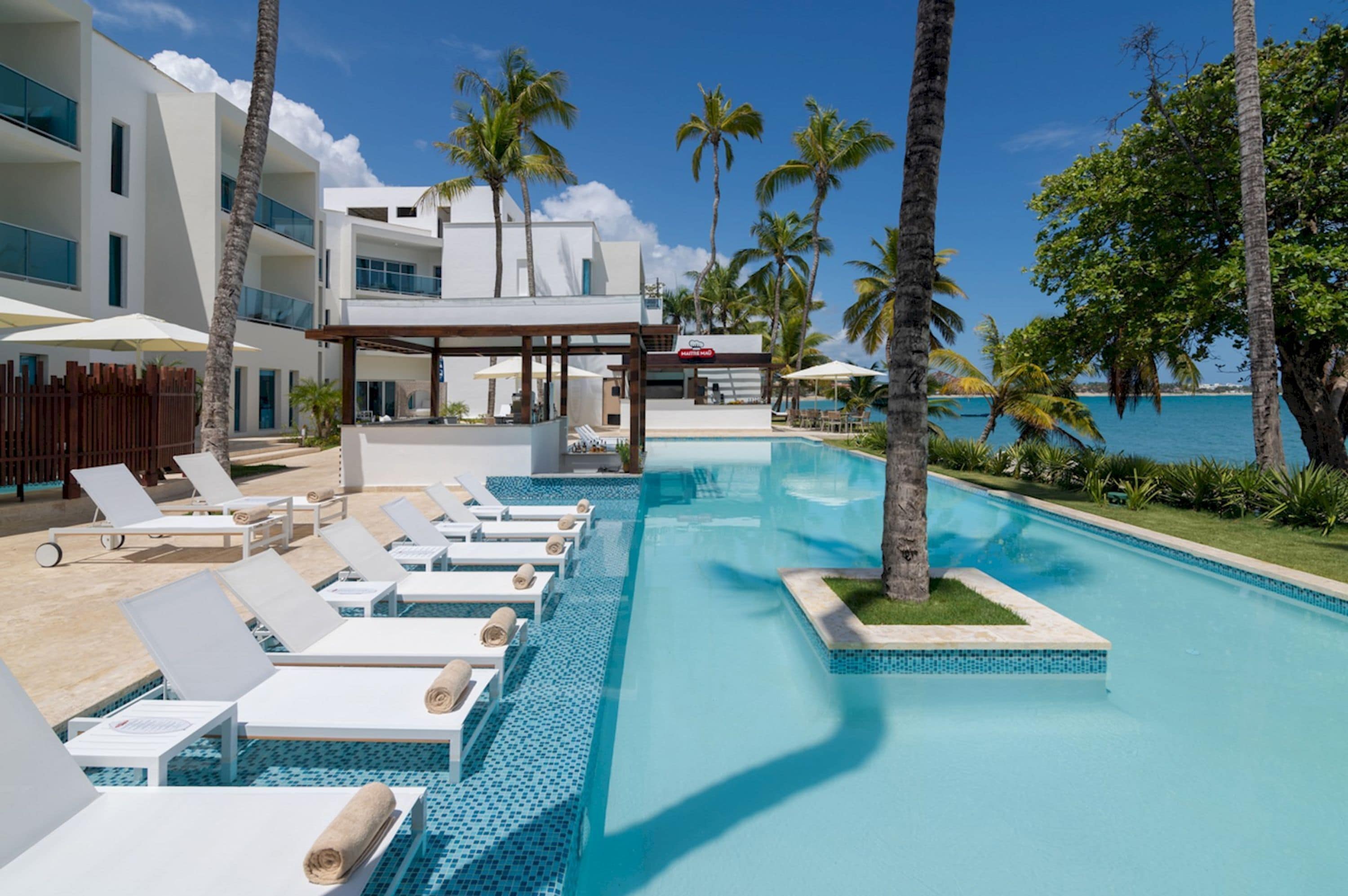 Un complexe hôtelier moderne doté d’une piscine, de chaises longues et offrant une vue sur l’océan.