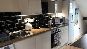 A modern kitchen with a washing machine, a microwave, and a built-in oven. - Windows Over Stroud Penthouse apartment with views (Stroud)