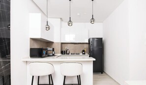 Une cuisine moderne dotée d’un îlot central, de deux tabourets de bar, d’un réfrigérateur noir et de luminaires suspendus.