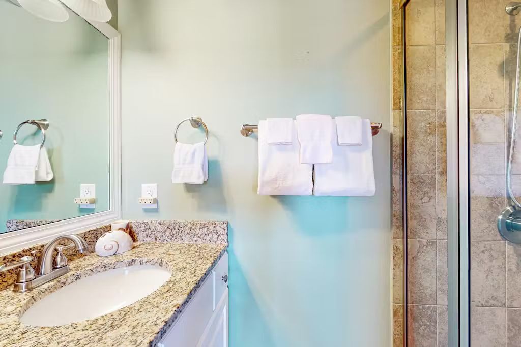 A bathroom with a granite countertop sink, a large mirror, and a glass shower enclosure.