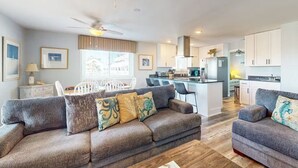 Un salon moderne avec un canapé gris, un coin repas avec des chaises blanches et une cuisine avec des meubles blancs.