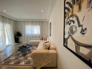 A modern living room with a beige sofa, a patterned rug, and a large abstract painting on the wall. - Le Relais: Apt de luxe à 5mn de la marsa (La Marsa)