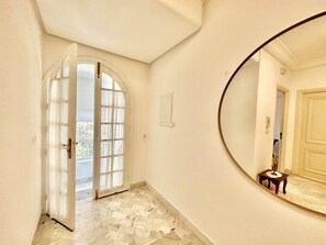 A hallway with a marble floor, a large mirror, and a door leading to a bright room. - Safran II Apt de charme avec Terrasse à la Marsa (Site archéologique de Carthage)