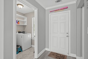 A laundry room with a washing machine and dryer, a small stool, and a shelf with cleaning supplies. - Relaxing Lowcountry Family Stay (Bluffton)
