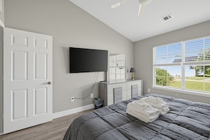 A bedroom with a bed, a TV mounted on the wall, a window with blinds, and a door. - Relaxing Lowcountry Family Stay (Bluffton)