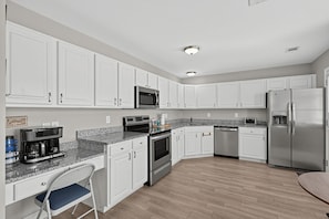 A modern kitchen with white cabinets, stainless steel appliances, a coffee maker, and a water dispenser. - Relaxing Lowcountry Family Stay (Bluffton)