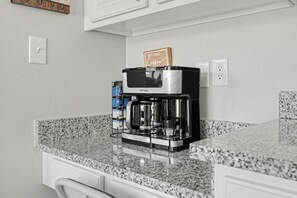 A kitchen with a coffee maker on a granite countertop, a wall-mounted light switch, and a sign that says 'BUT FIRST... Coffee.' - Relaxing Lowcountry Family Stay (Bluffton)