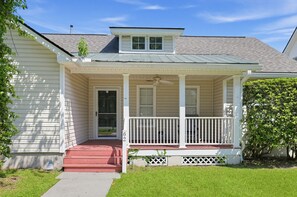 Een gelijkvloers huis met een veranda, een schoorsteen en een kleine tuin.