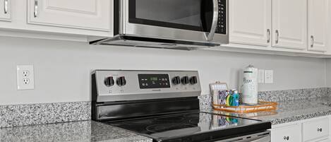 A kitchen with a stainless steel microwave, a stove, and a refrigerator.
