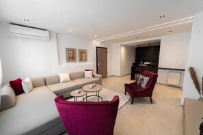 A modern living room with a sofa, a red chair, a coffee table, and a kitchen area in the background. - SUNSET 201: Luxury 2bds with gym (Tunis)