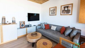 Una sala de estar moderna con un sofá gris, una mesa de centro de madera y un televisor de pantalla plana montado en la pared.