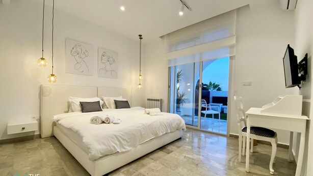 A modern bedroom with a large bed, a desk, and a view of the outdoors. - New 1 bd with garden and sea side at Marsa Cornich (Site archéologique de Carthage)