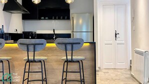 A modern kitchen with black cabinets, a stainless steel refrigerator, and a bar area with stools. - New 1 bd with garden and sea side at Marsa Cornich (Site archéologique de Carthage)