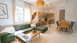 Ein modernes Wohnzimmer mit einem grünen Sofa, einem Esstisch mit Stühlen und einer Küche im Hintergrund.
