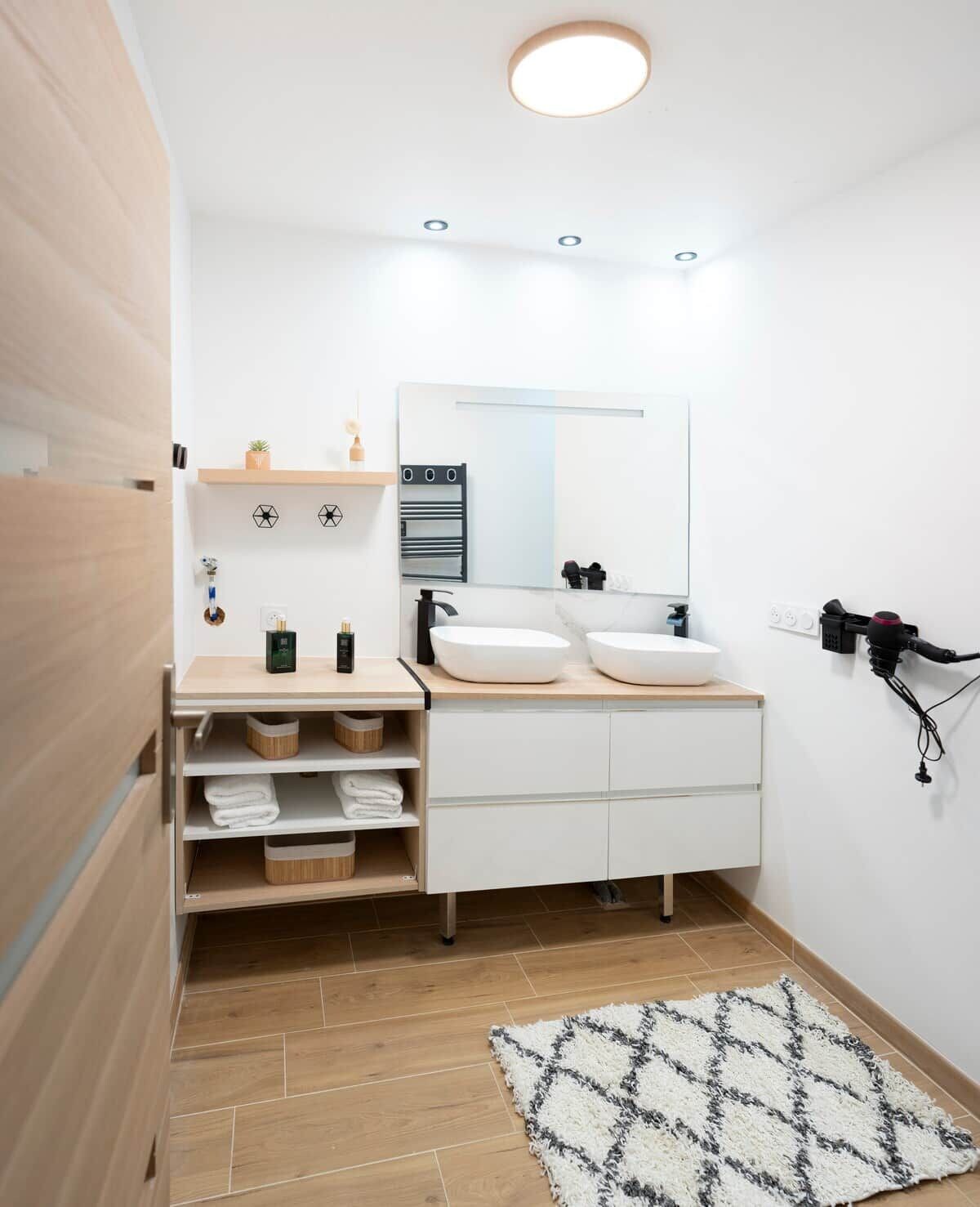 A modern bathroom with a white vanity, two sinks, a mirror, and a towel rack.