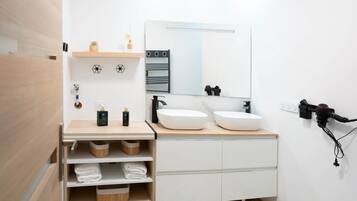 A modern bathroom with a white vanity, two sinks, a mirror, and a towel rack.