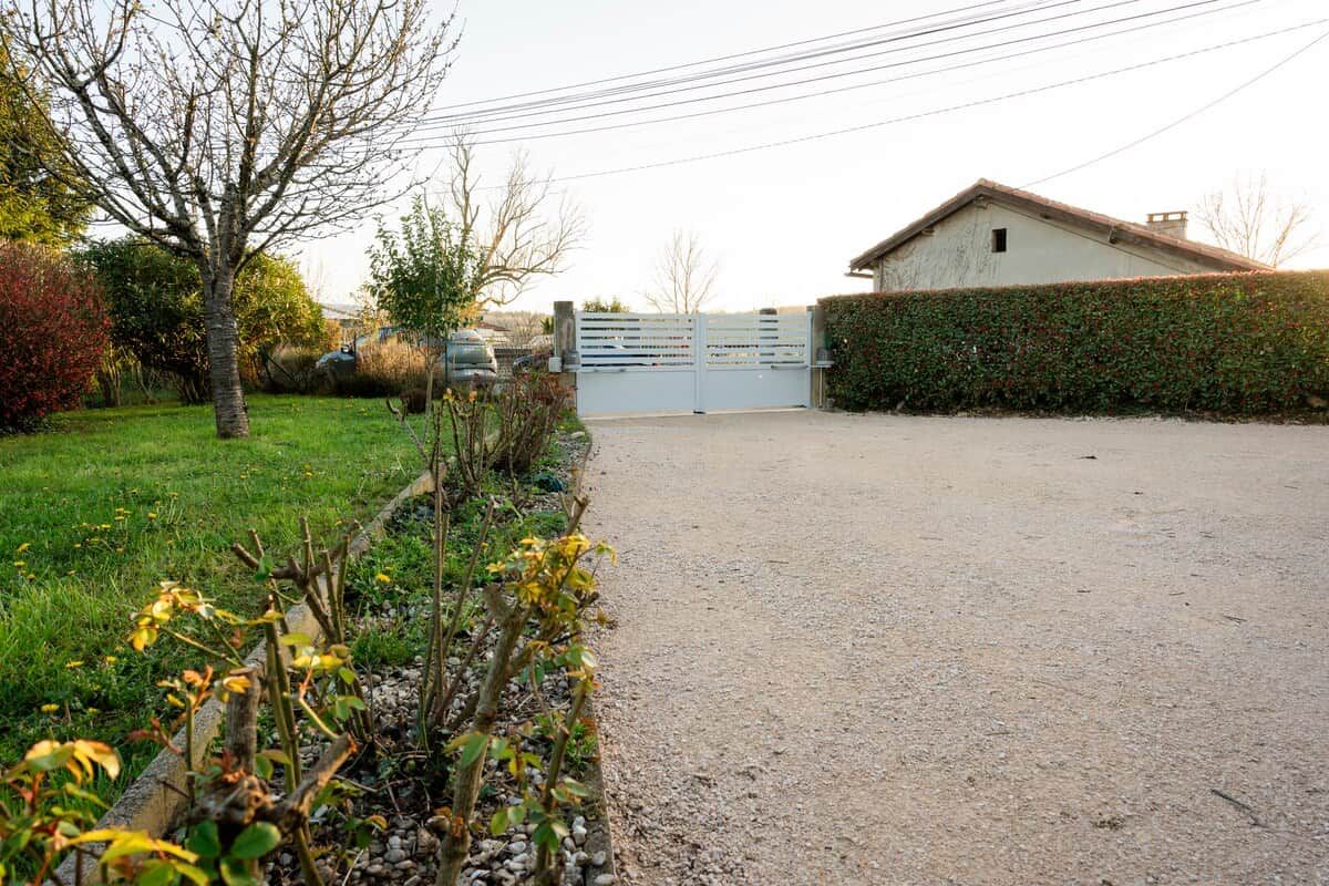 A gravel driveway leading to a gated entrance with a building on the right.