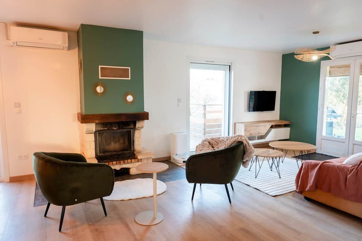 Ein modernes Wohnzimmer mit Kamin, zwei Sesseln, einer Couch und einem Fernseher, sowie einem großen Fenster.