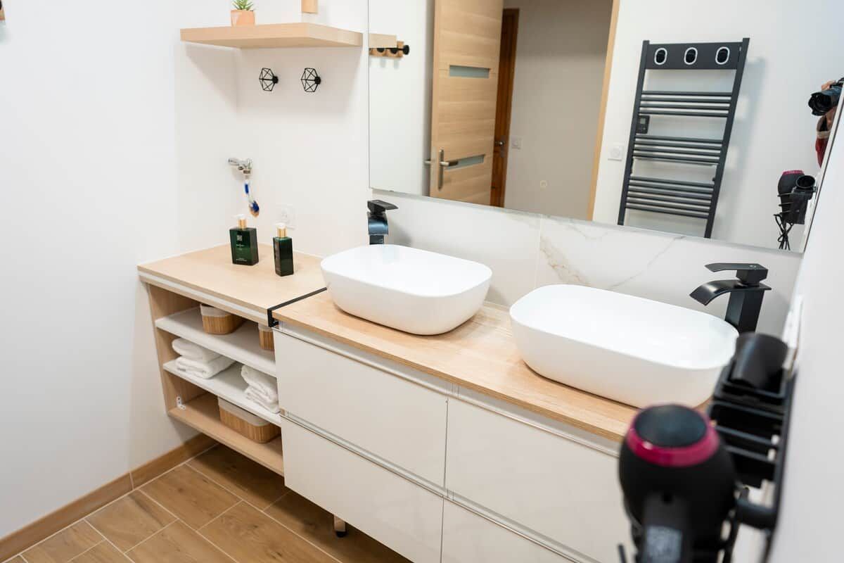 A modern bathroom with two sinks, a mirror, and a towel rack.