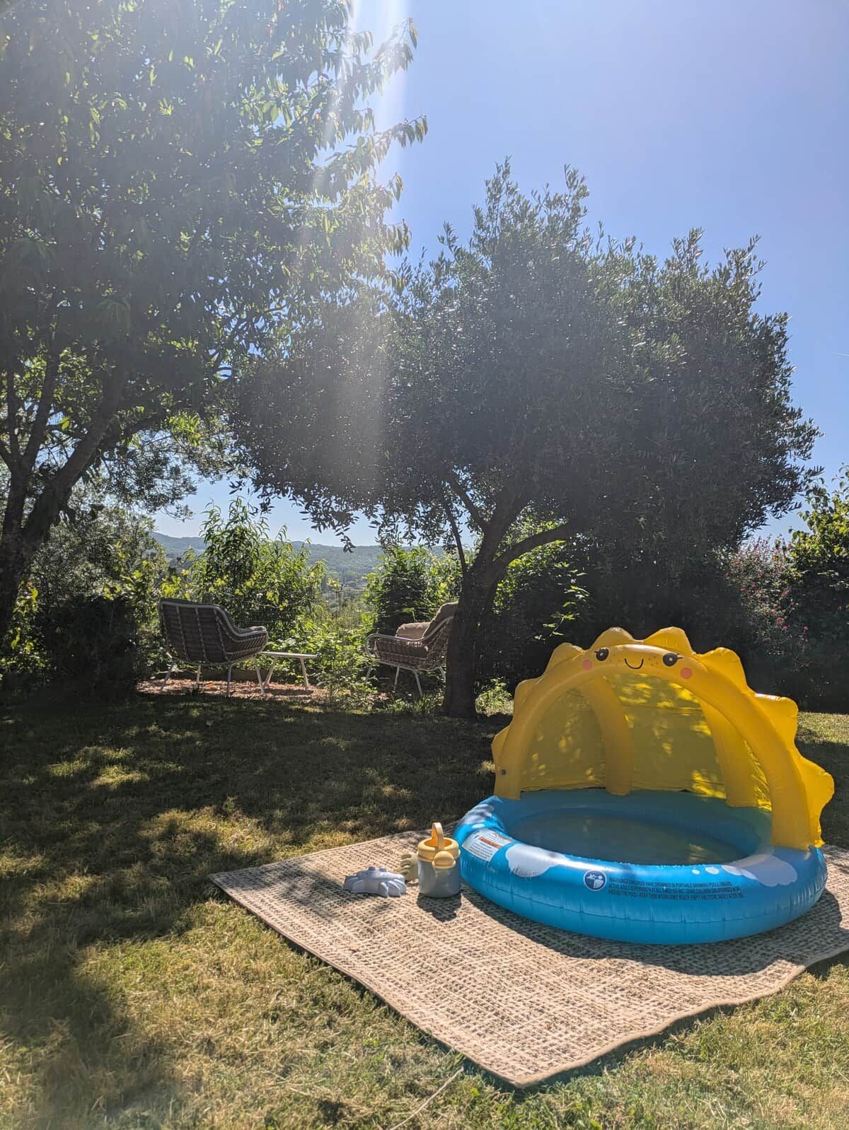 Ein aufblasbarer Pool mit Hai-Motiv, umgeben von Bäumen und einer Rasenfläche mit Picknickplatz.