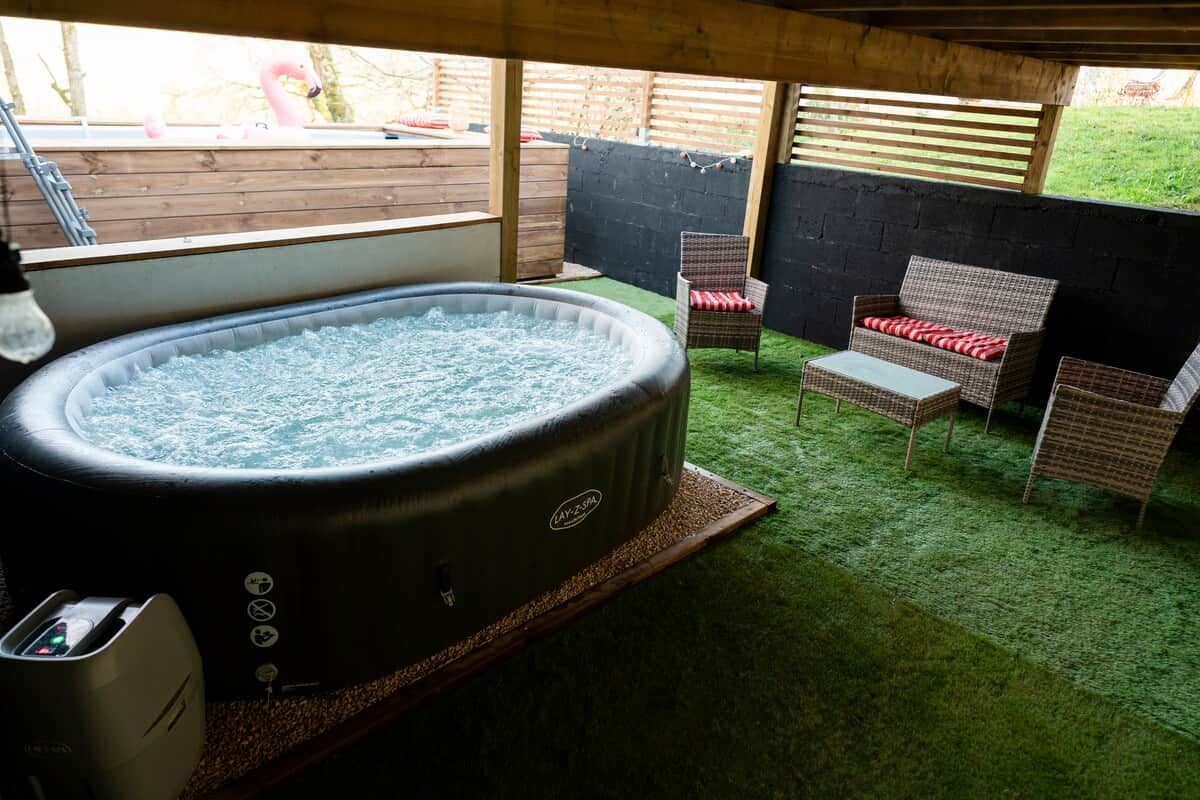 Un bain à remous équipé de commandes, entouré de fauteuils en osier et d’une terrasse en bois.
