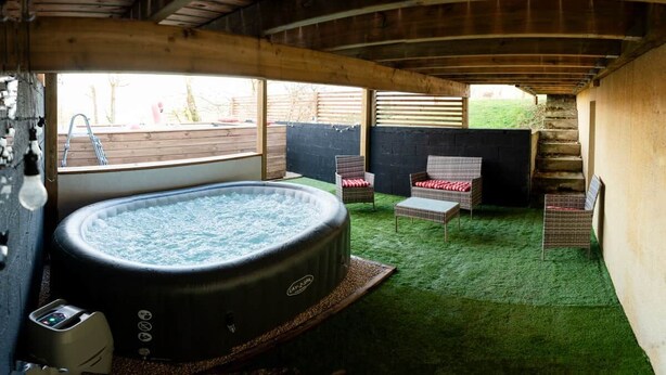A hot tub in a wooden room with a green carpet, a chair, and a small table. - A Getaway in the Pyrenees: Views, Hot Tub, and Forest (Marseillan)