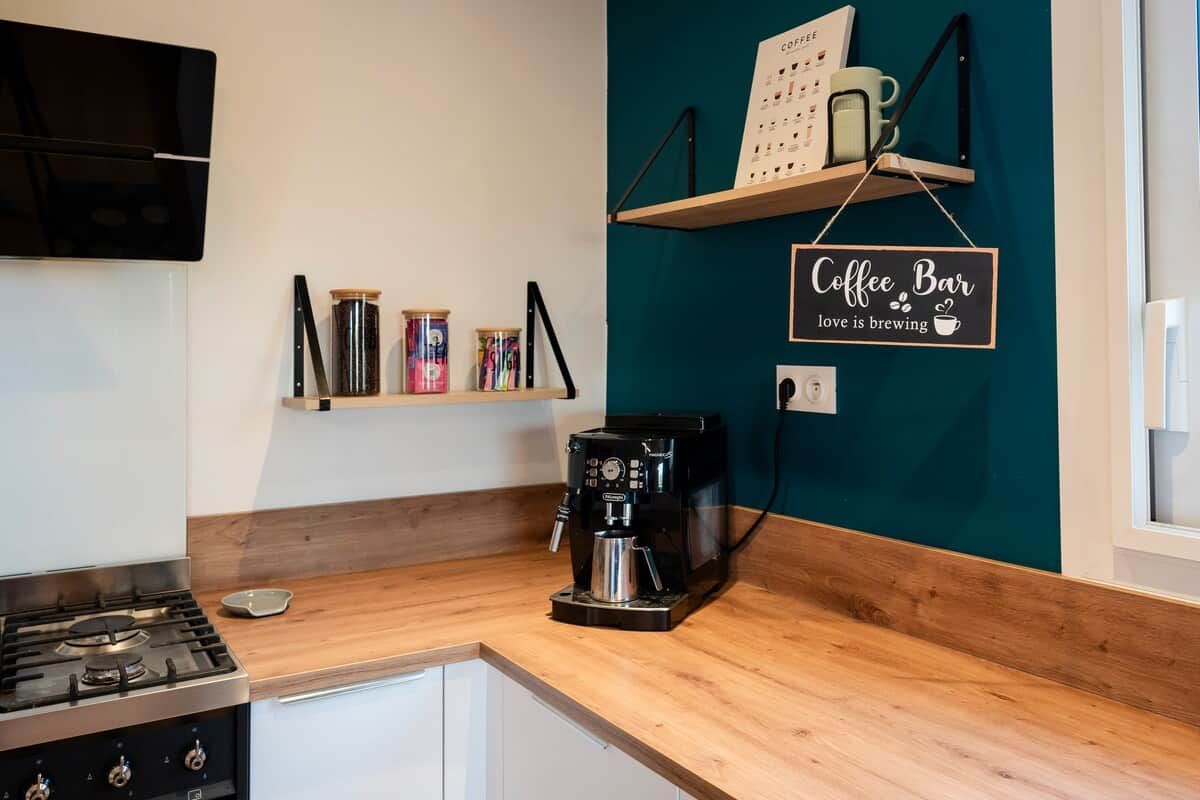 A kitchen with a coffee machine, a stove, and a shelf with coffee mugs.