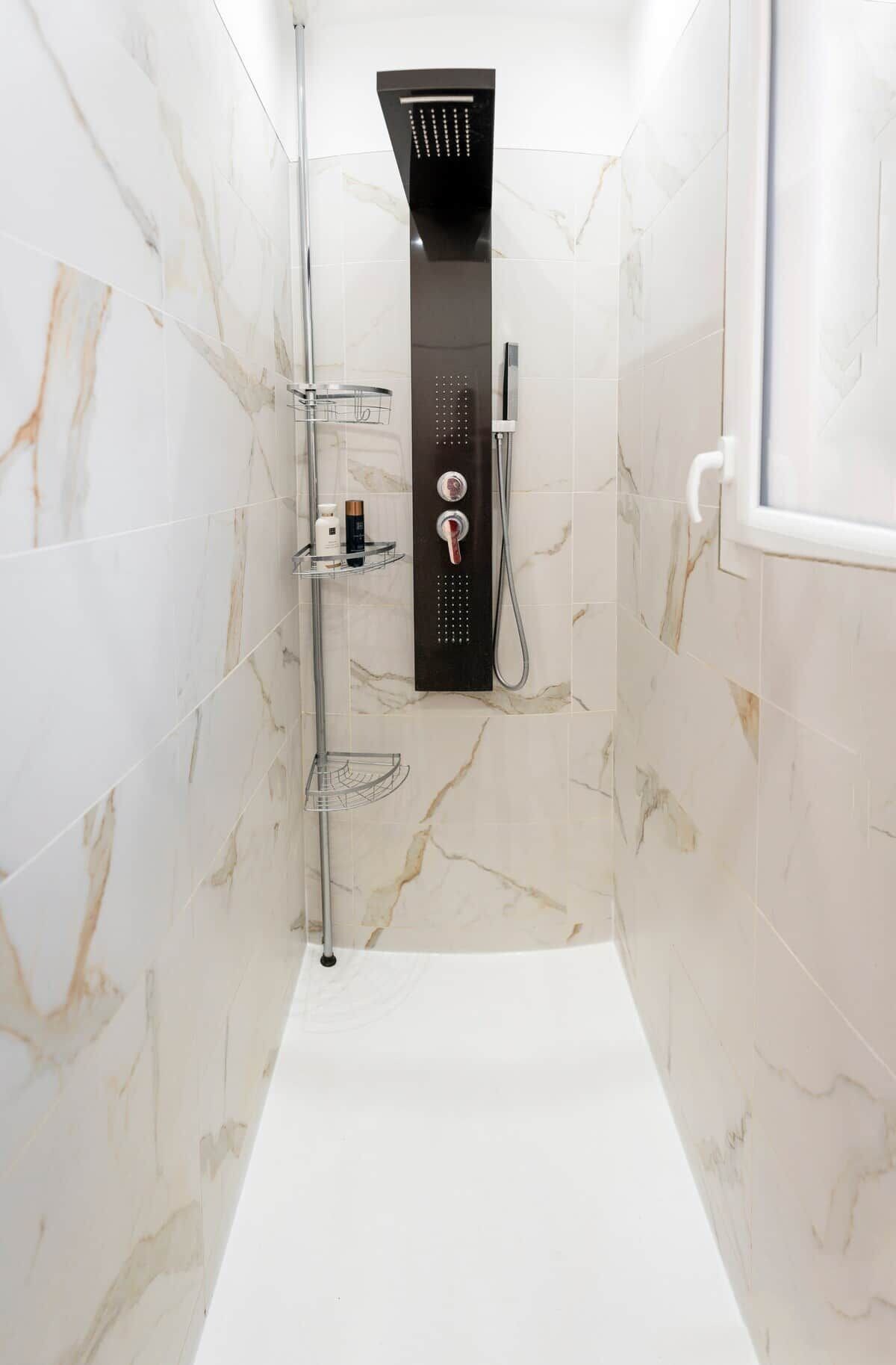 Un baño moderno con ducha, paredes de mármol y una bañera blanca.