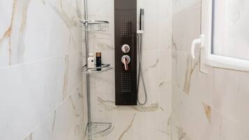 Un baño moderno con ducha, paredes de mármol y una bañera blanca.