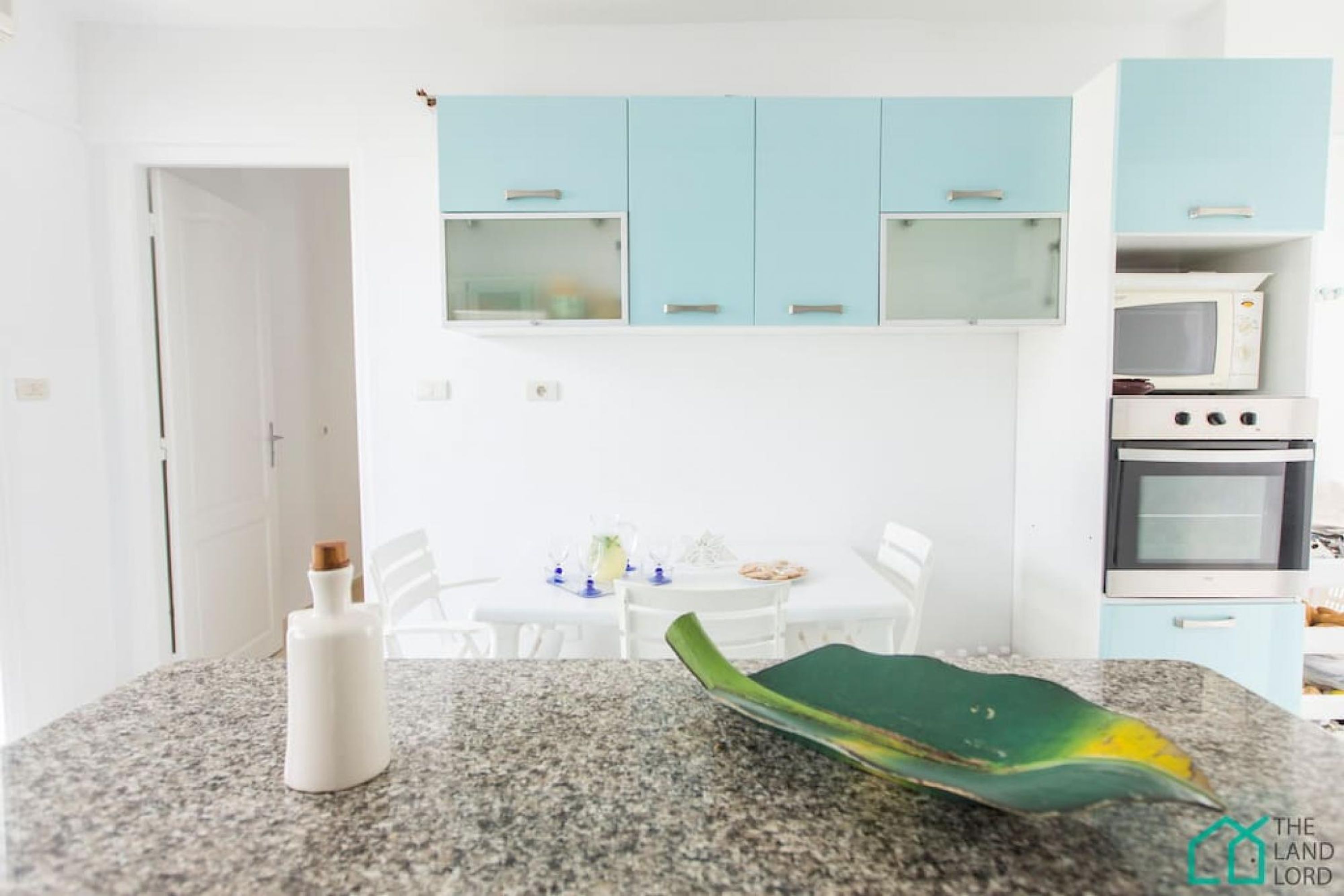 Une cuisine avec des comptoirs en granit, une bouteille blanche et une feuille verte. Des armoires bleu clair se trouvent au-dessus du comptoir.