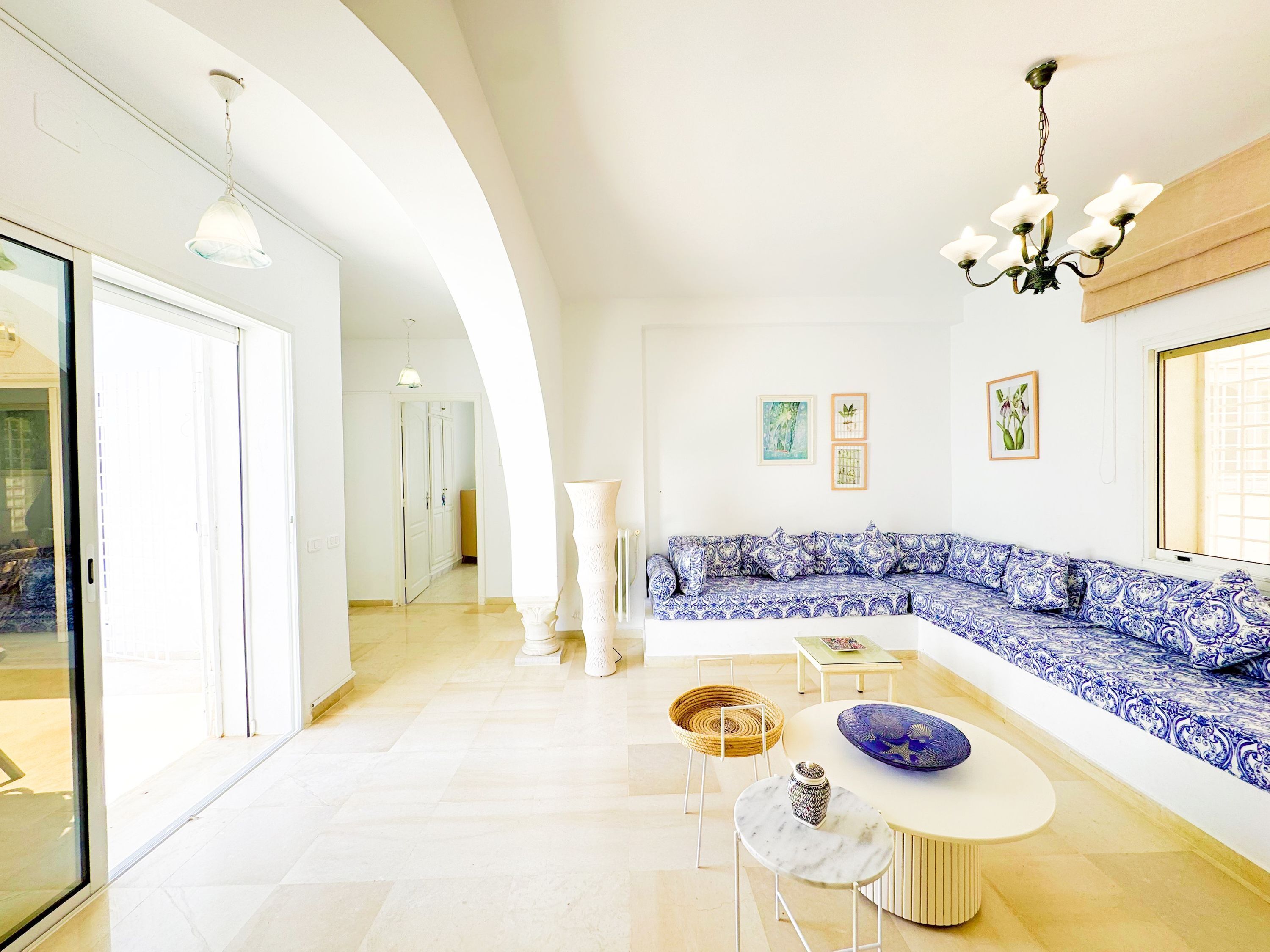 Un salon spacieux avec un canapé bleu à motifs, une table basse ronde et un lustre.