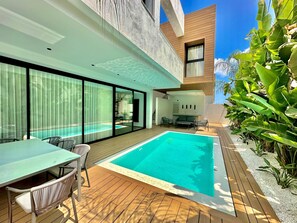 Ein moderner Poolbereich im Freien mit Holzterrasse, einem Esstisch mit Stühlen und einer Lounge mit Sofas.