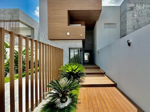 Ein modernes architektonisches Design mit einer Holterrasse, einer Betonwand und einem kleinen Gartenbereich mit Pflanzen.