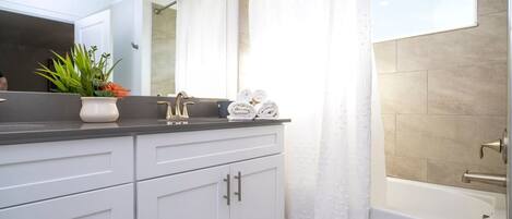 Un baño con bañera, lavamanos con espejo y una planta en maceta.