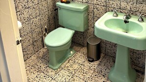 A compact bathroom with a toilet, sink, and a framed picture on the wall. - Mid century bungalow mins to Pearl, dt, airport (San Antonio)