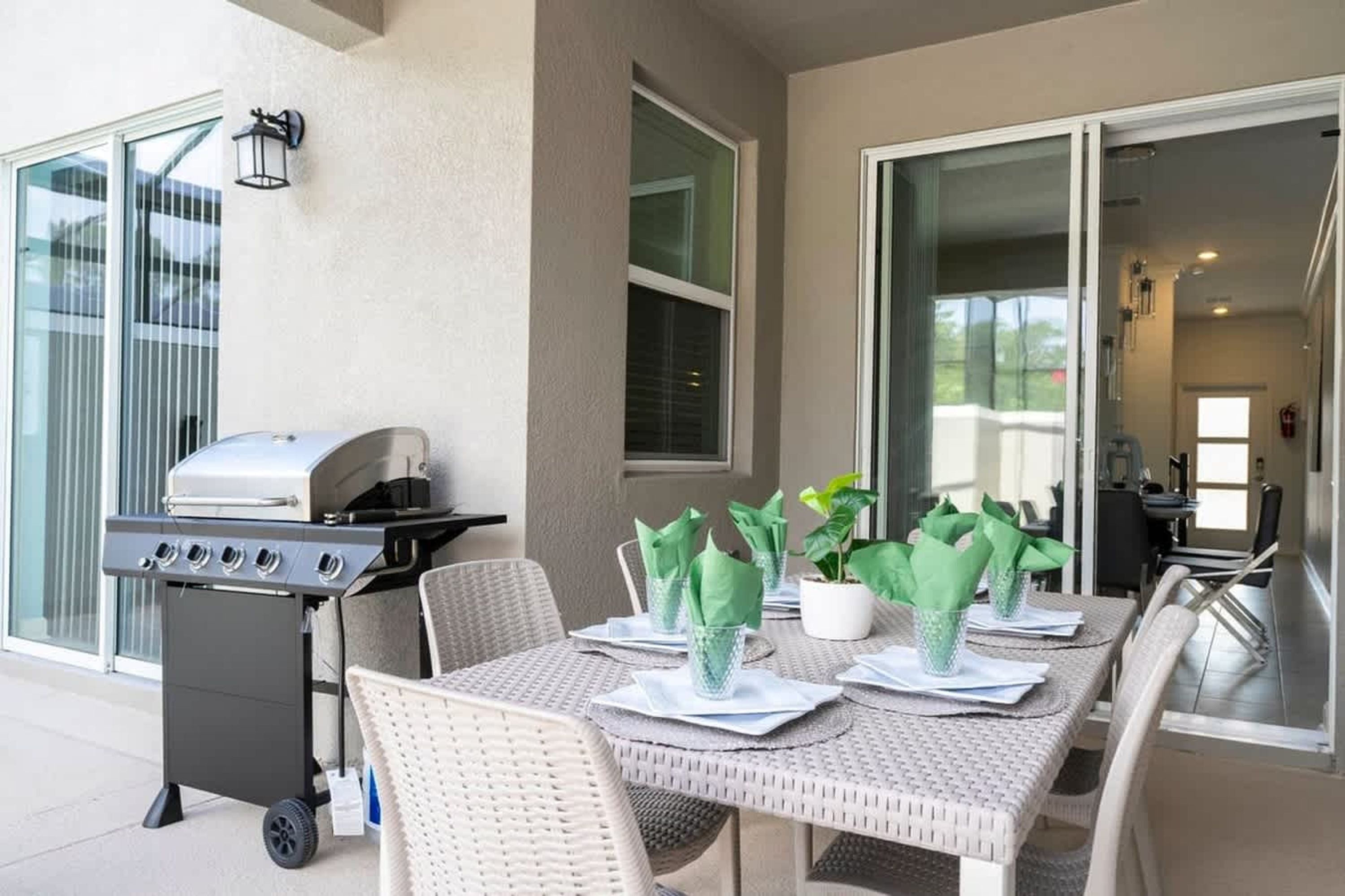 An outdoor patio with a grill, wicker chairs, a table set with green napkins, and a potted plant.