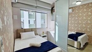 A hotel room with a bed, bedside table, and a mirror reflecting the room. - COBAR0148 - Edifício Beta (Salvador)