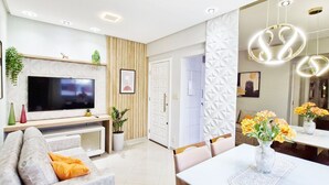 A modern living room with a flat-screen TV, a sofa, a dining table, and a decorative vase. - COBAR0148 - Edifício Beta (Salvador)